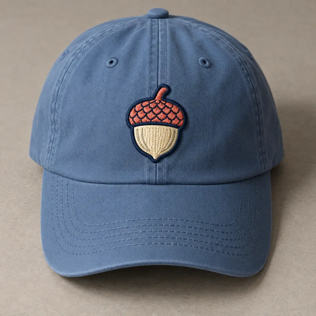 Embroidered acorn patch on the front of a blue dad cap.