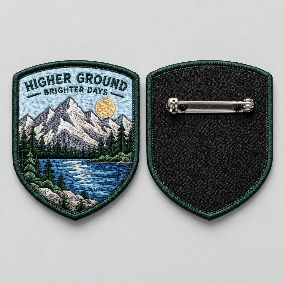 Embroidered Higher Ground shield patch beside its back with a brooch pin.