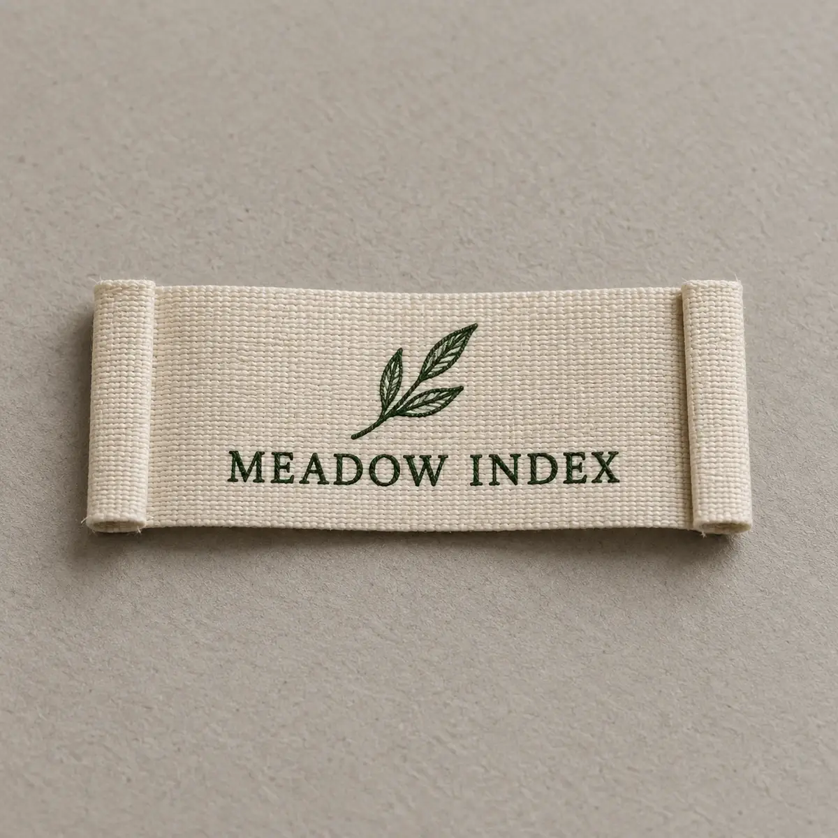 Cream end-fold woven label reading Meadow Index with a leaf.