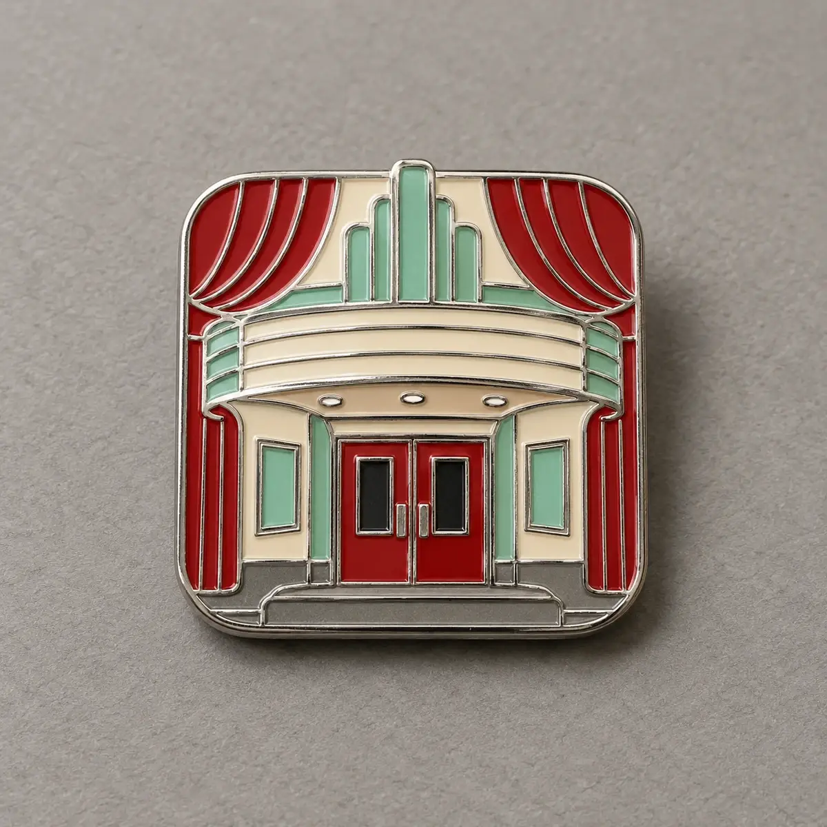 Silver enamel pin of an art deco theater with red curtains.