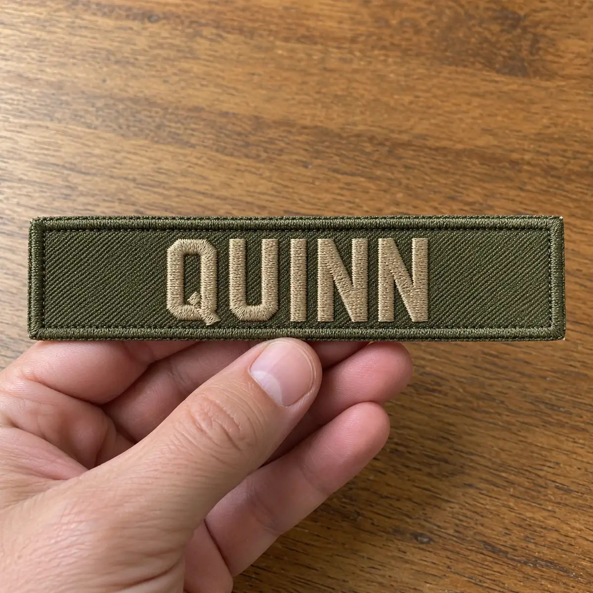 Olive embroidered QUINN name tape held in hand.