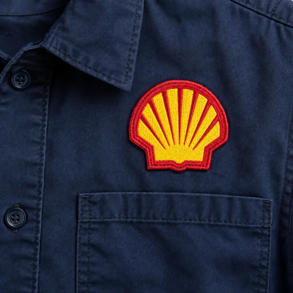 Embroidered yellow and red shell logo patch on a navy work shirt.