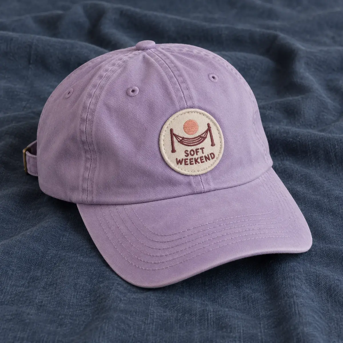 Round embroidered Soft Weekend hammock patch on a lilac cap.