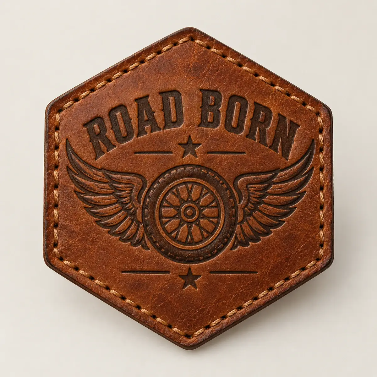 Laser-engraved hexagonal Road Born leather patch with a winged wheel.