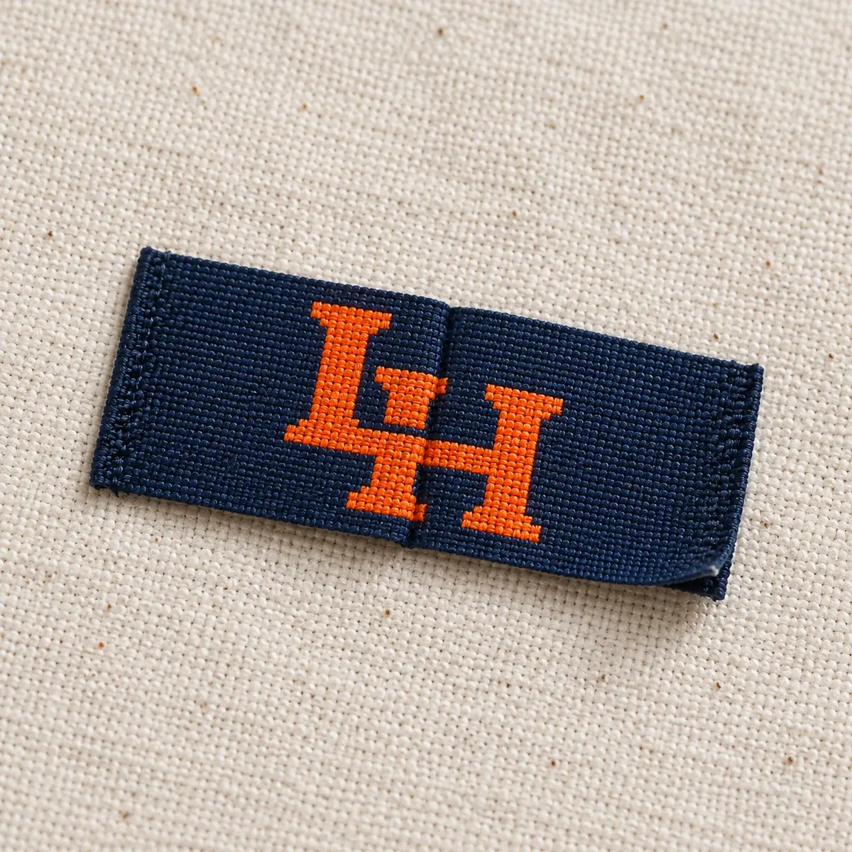 Navy folded woven label with an orange LH monogram.
