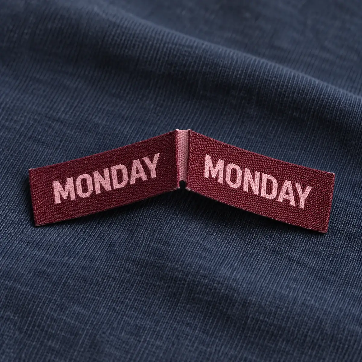 Burgundy loop-fold woven label reading Monday on navy knit.