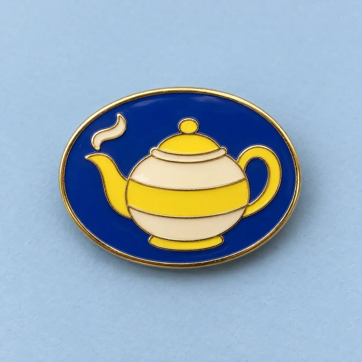 Oval navy enamel pin with a yellow striped teapot.