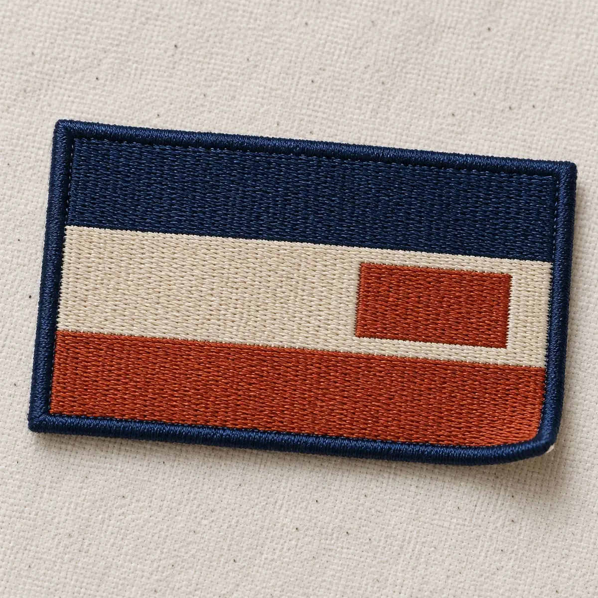 Embroidered navy, cream and rust flag patch with a merrow border.