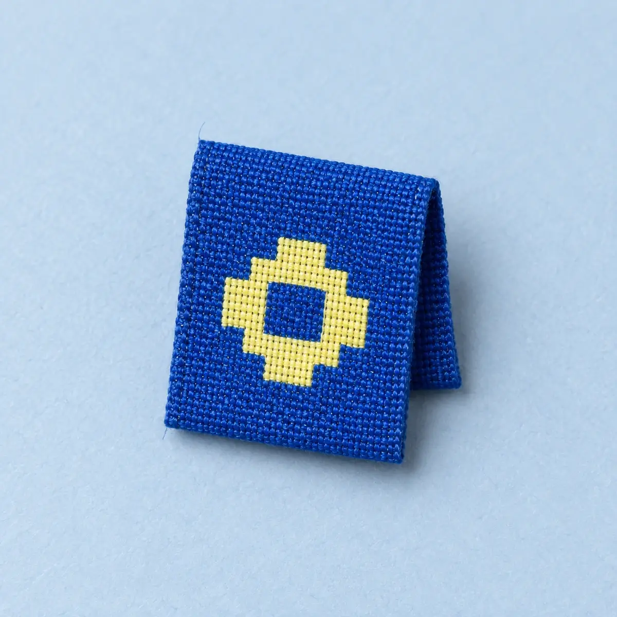 Folded blue woven tag with a yellow pixel ring.