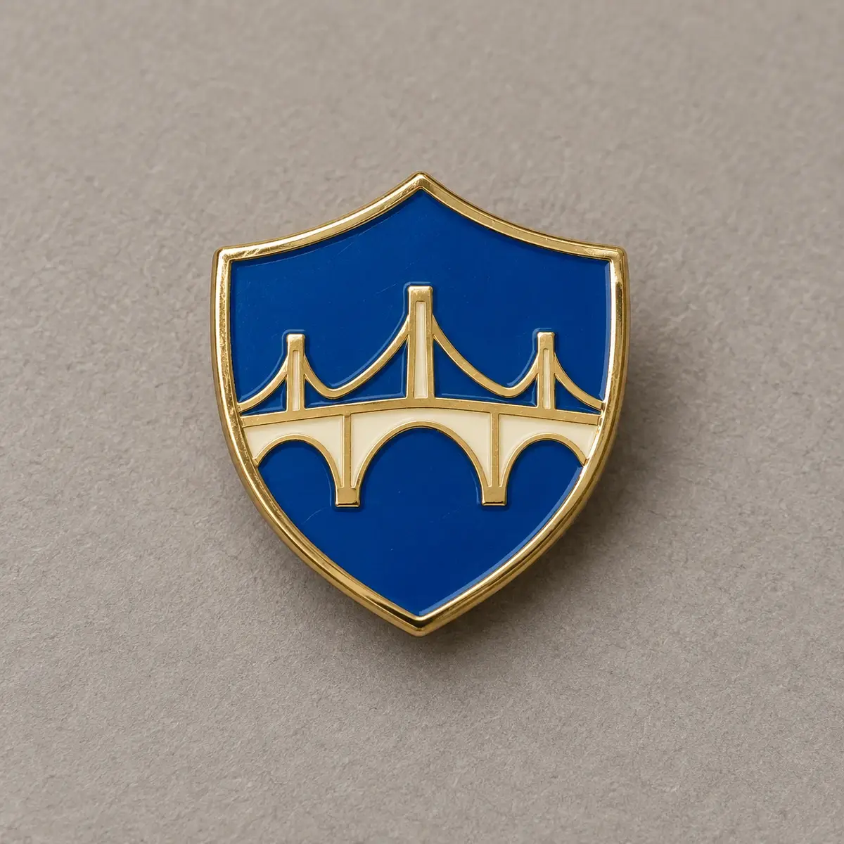 Blue shield enamel pin with a cream bridge and gold edges.