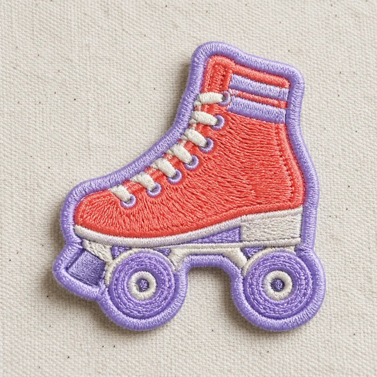 Embroidered coral and lavender roller skate patch on canvas.