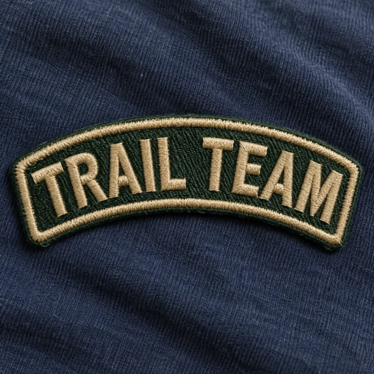 Green embroidered Trail Team rocker patch on navy fabric.