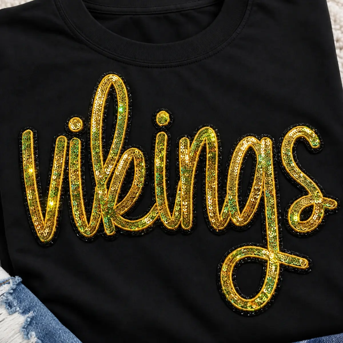 Gold sequin Vikings script patch on a black shirt.