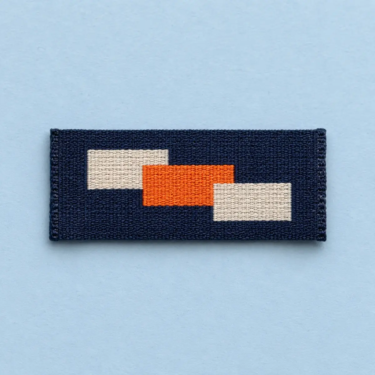 Woven rectangular patch with orange and cream blocks on navy.