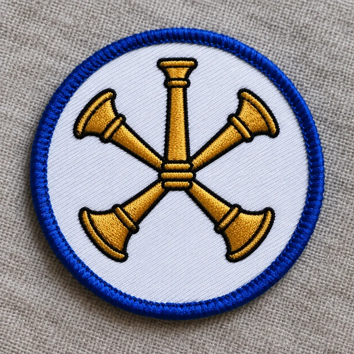 Round embroidered patch with four crossed gold fire bugles on white.