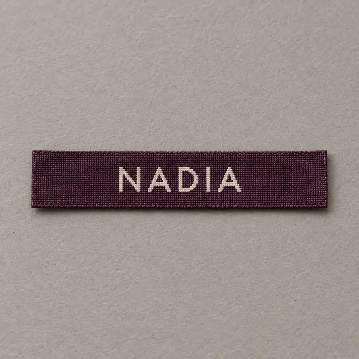 Burgundy woven name label reading NADIA.