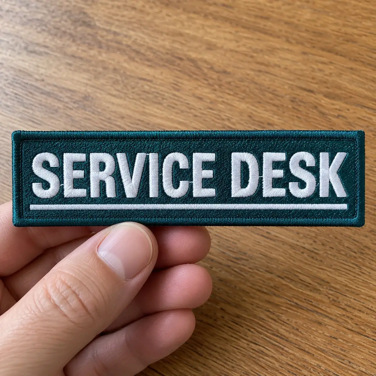 Teal embroidered SERVICE DESK name tag held in hand.